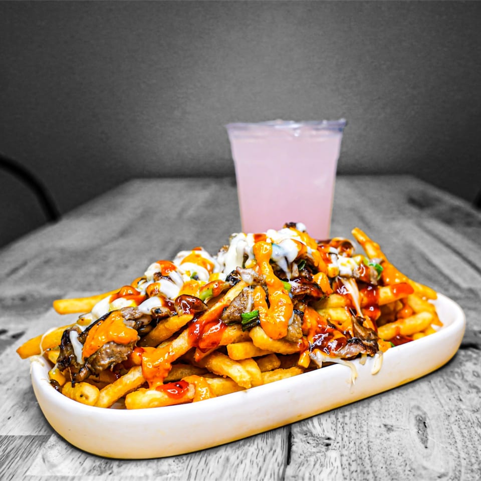 A white platter of KK'S FRIES loaded with meat, cheese, and sauces, with a pink drink.