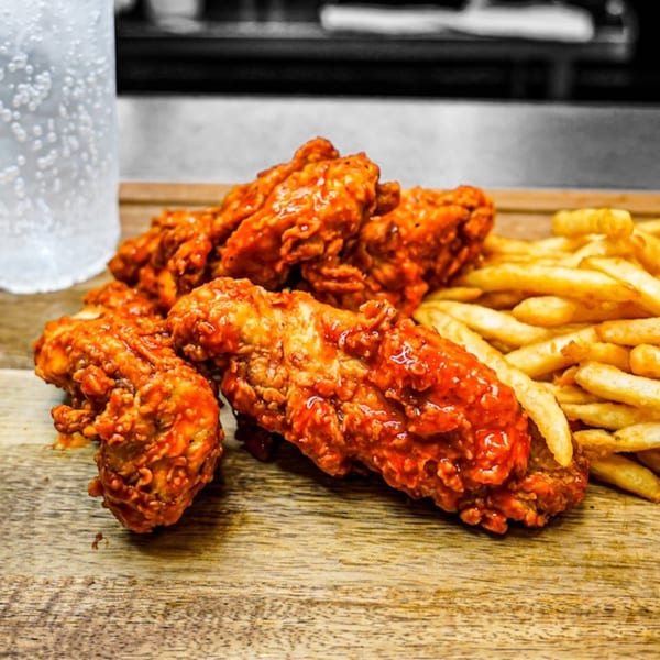 Spicy chicken tenders and golden french fries on a wooden board with a bubbly drink.
