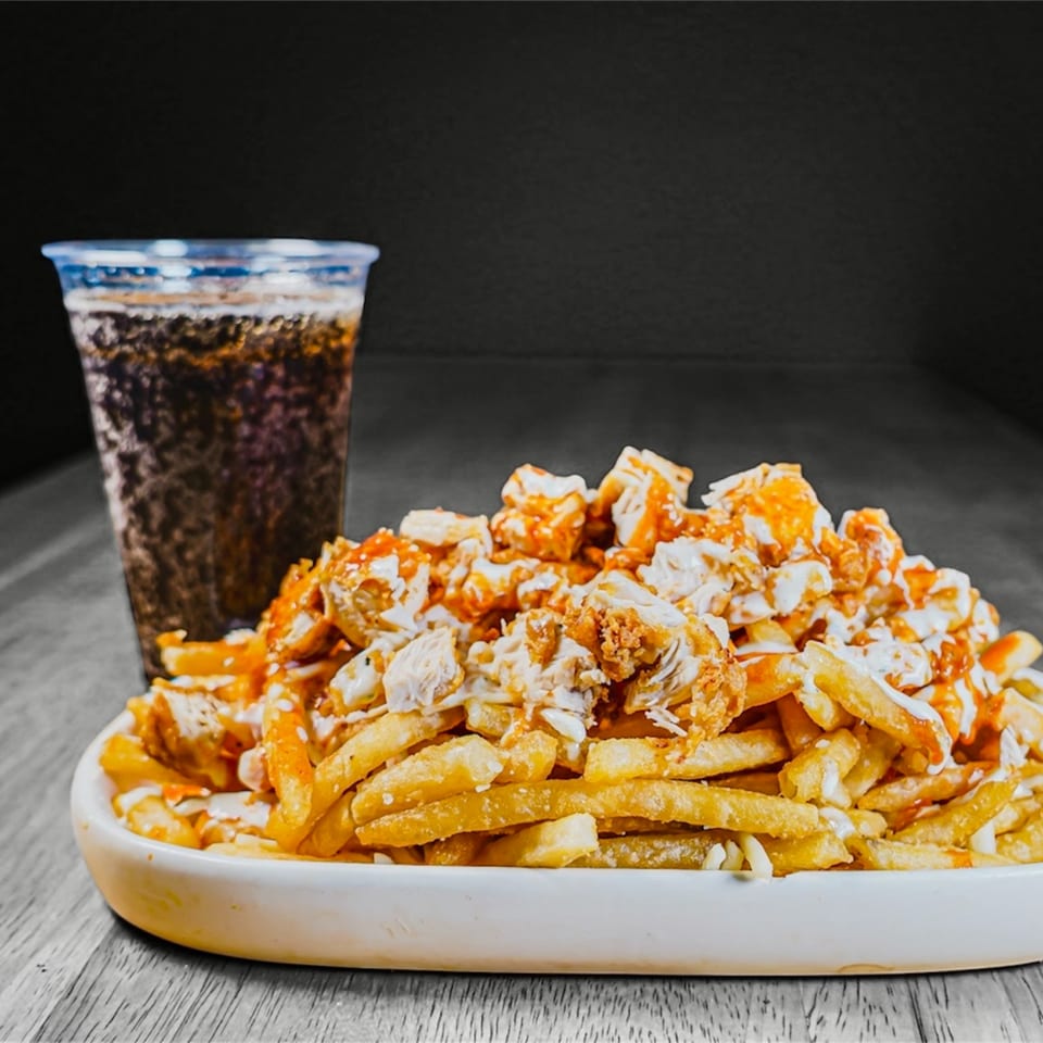 A plate of KK'S FRIES with chicken, sauces, and a soda drink on a wooden table.