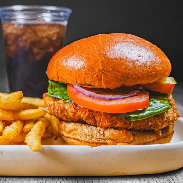 Crispy chicken sandwich with lettuce, tomato, onion, pickles, fries, and a soda.