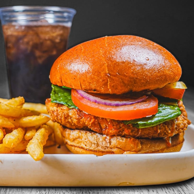 Crispy chicken sandwich with lettuce, tomato, onion, pickles, fries, and a soda.