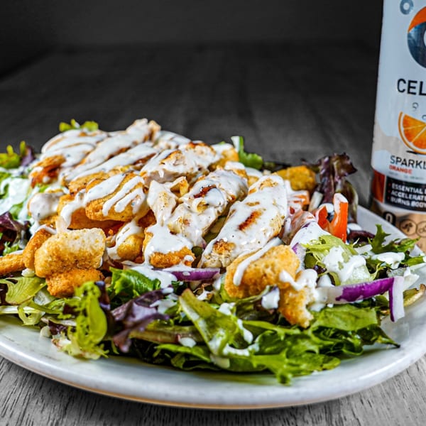 A vibrant salad with grilled chicken, croutons, and ranch dressing, next to a sparkling orange drink.