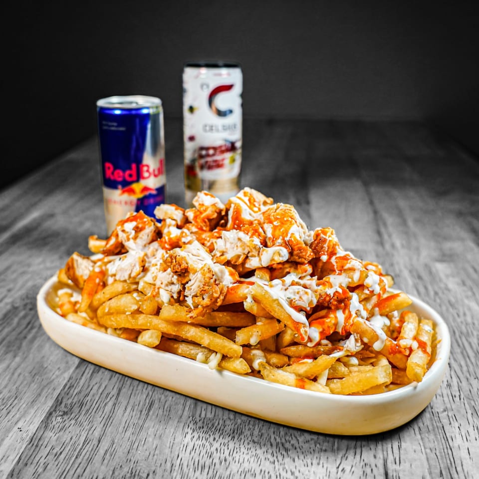 KK'S FRIES loaded fries with chicken, sauces, and two energy drink cans on a wooden table.