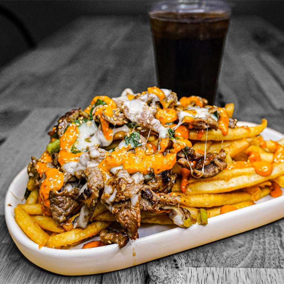 KK'S FRIES loaded fries with steak, melted cheese, orange sauce, and a drink.